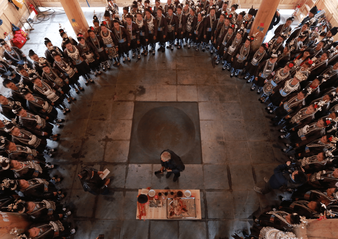 Aerial view of villagers in traditional dress gathered in a large circle in the village