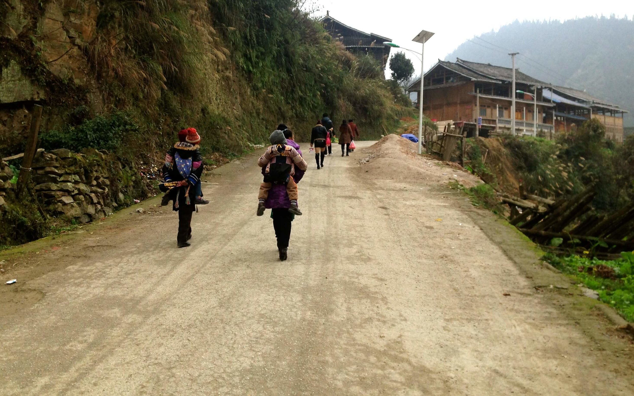 Villagers carrying loads along a dirt road into the village